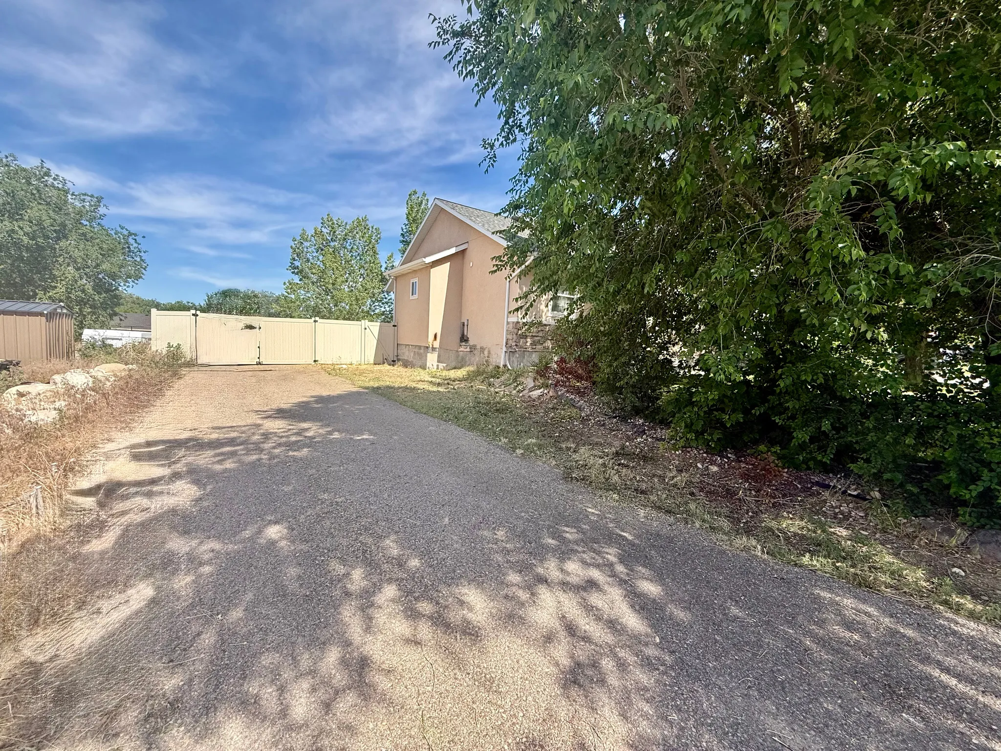 Gravel driveway with a tan vinyl privacy fence and gate