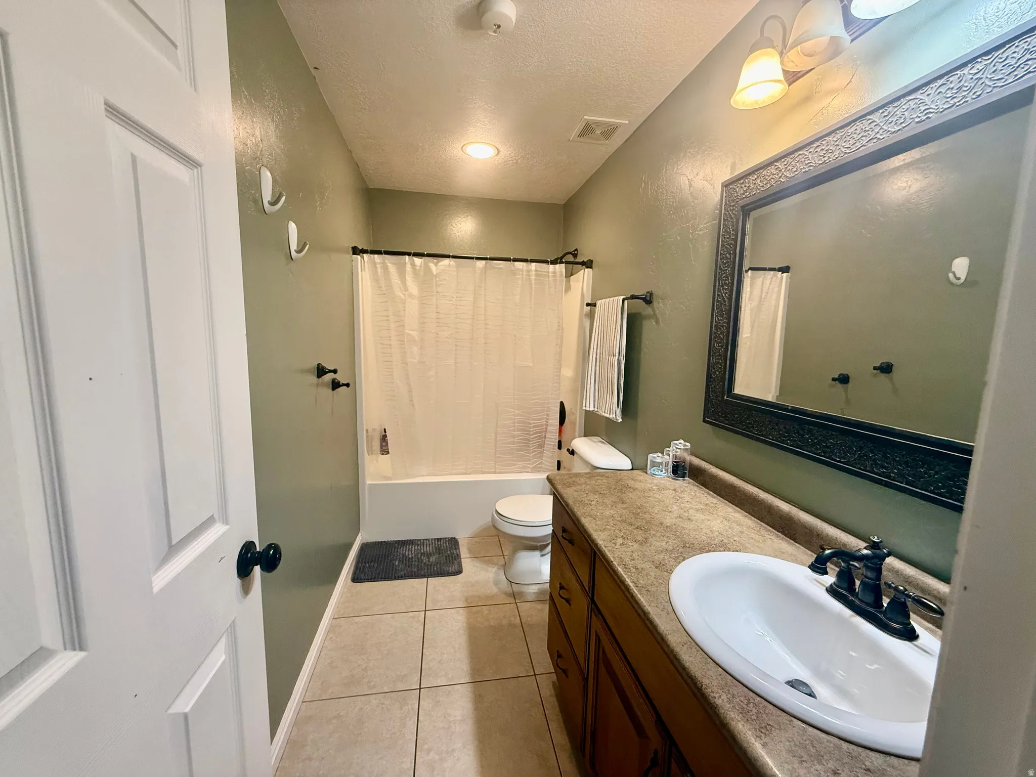 Full bathroom featuring a single vanity with a laminate countertop, an ornate framed mirror, a tub/shower combination, and tile flooring