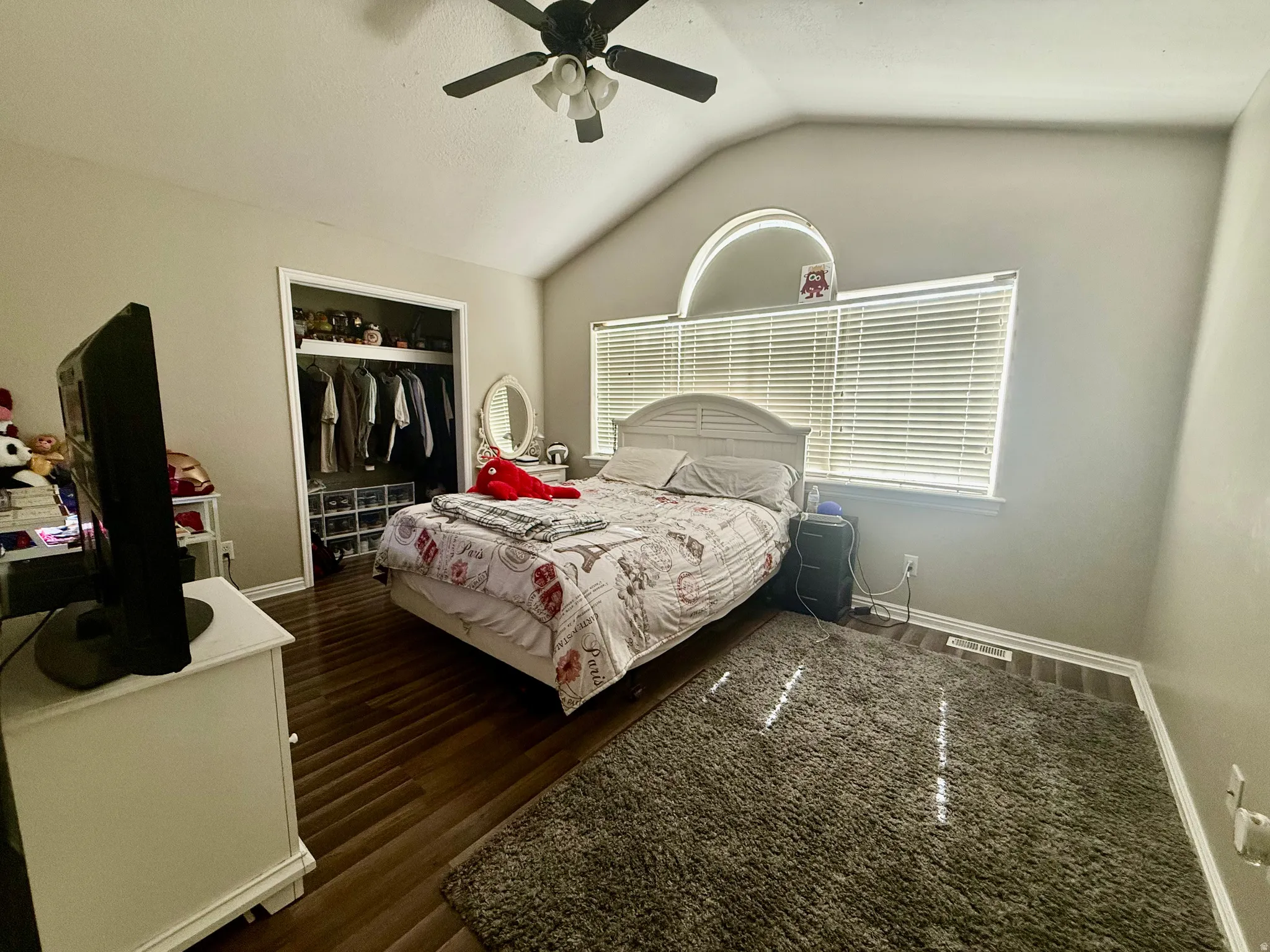 Vaulted ceilings featuring a ceiling fan with light kit, a large window with blinds, and wood-finish flooring