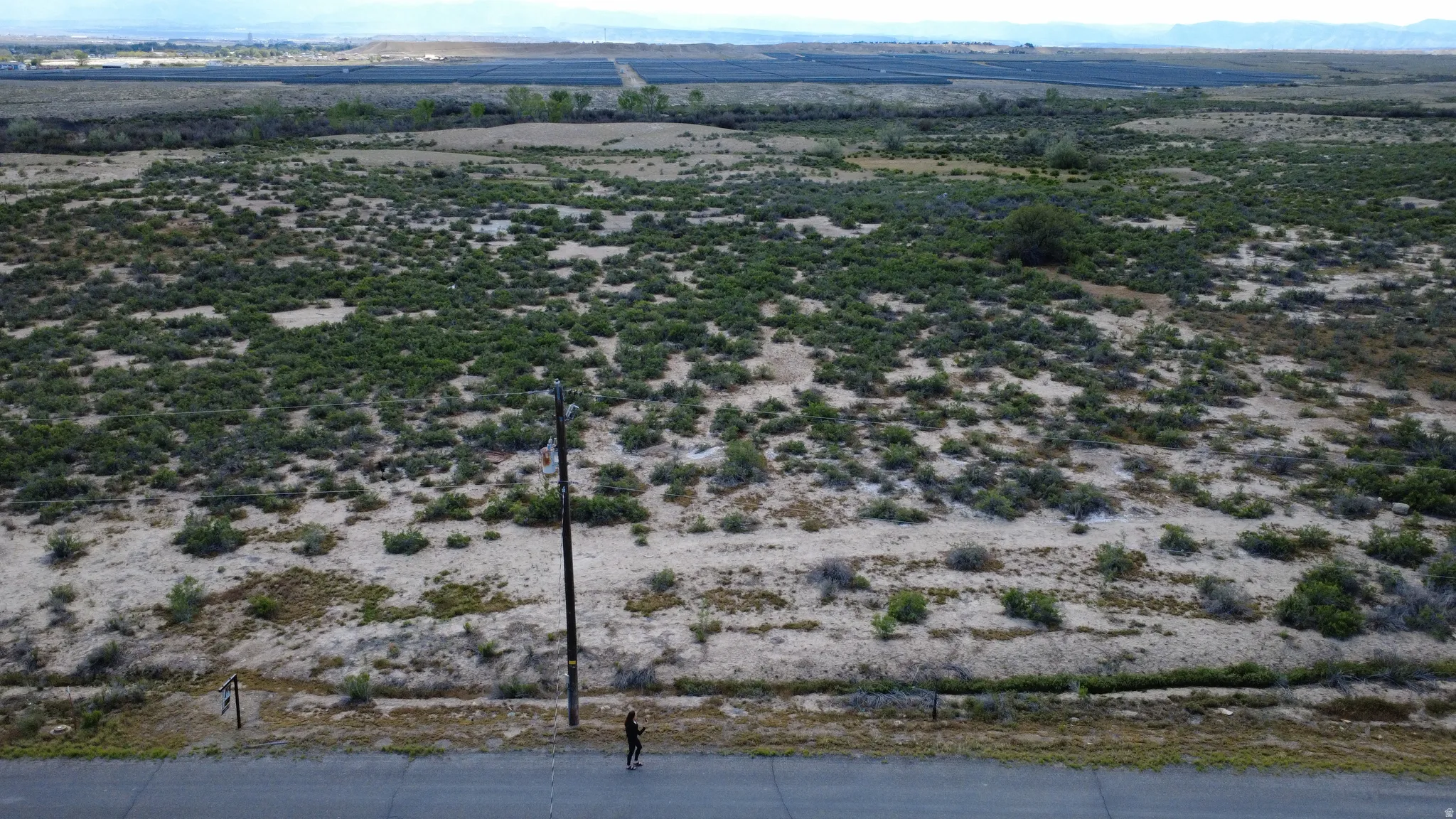 Expansive land parcel featuring natural shrubbery and a paved road frontage