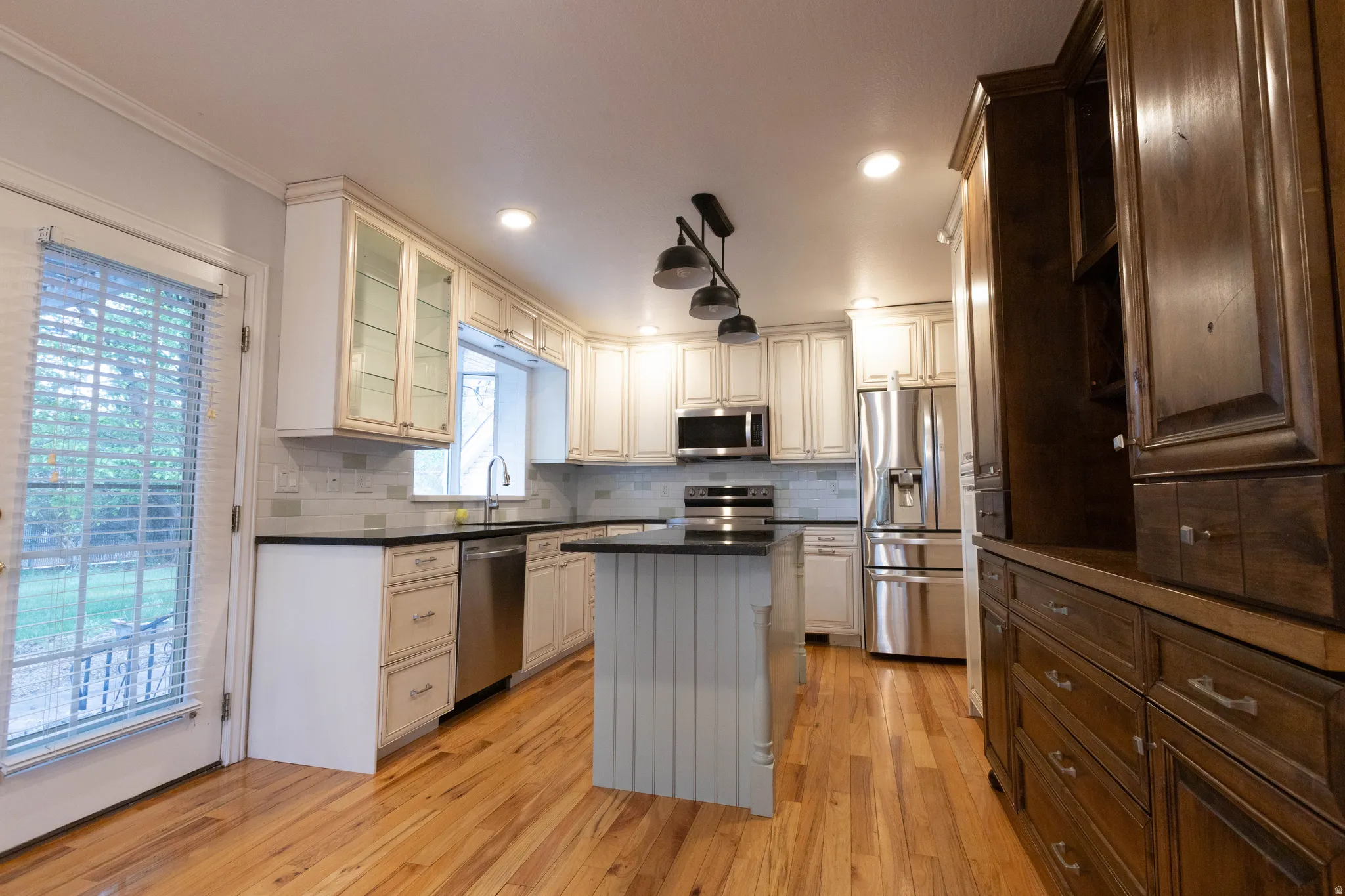 Kitchen with light wood-finish flooring, two-tone cabinetry, stainless steel appliances, dark countertops, and a full tile backsplash