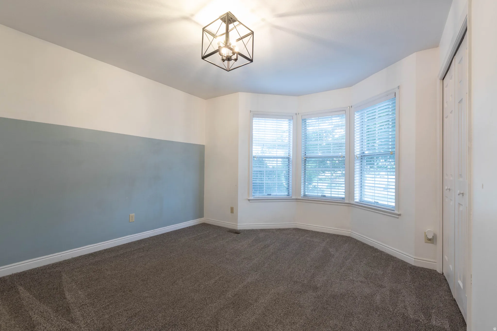 Bay window with three individual pane windows, a modern geometric ceiling light fixture, bi-fold closet doors, and textured carpeting