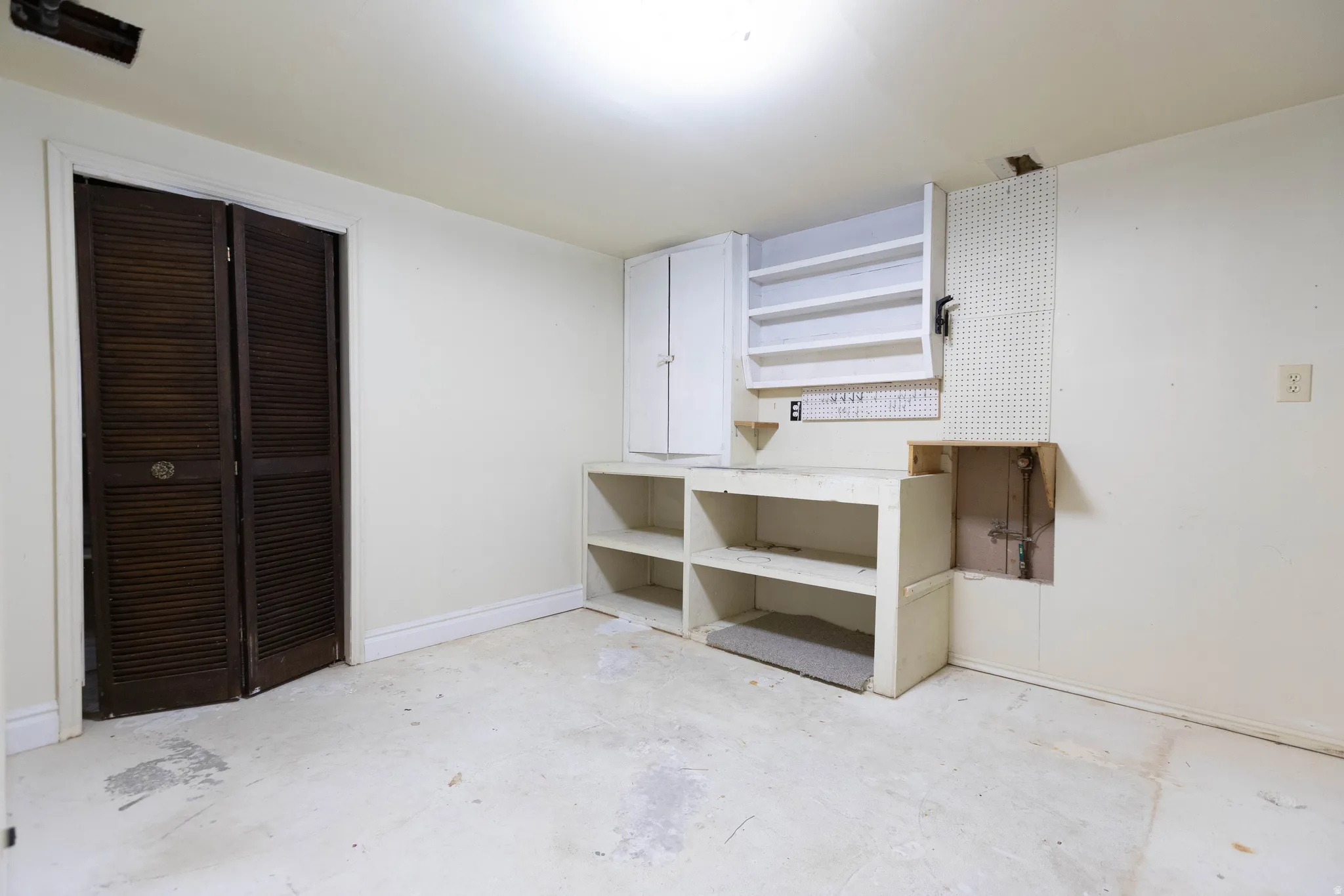 Utility area featuring built-in shelving, white cabinetry, louvered closet doors, and exposed pegboard for organization