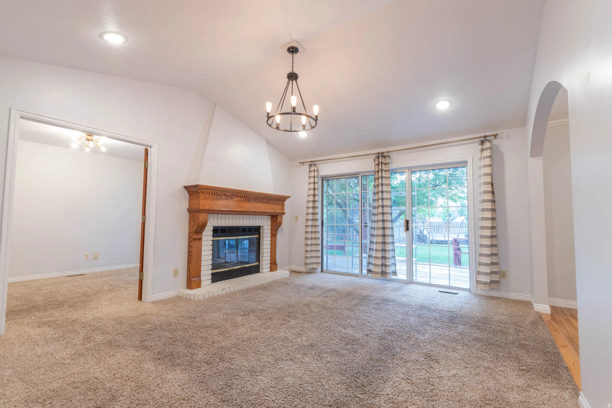 Spacious living area featuring a vaulted ceiling, recessed lighting, and a prominent fireplace with a carved wood mantel and white brick surround