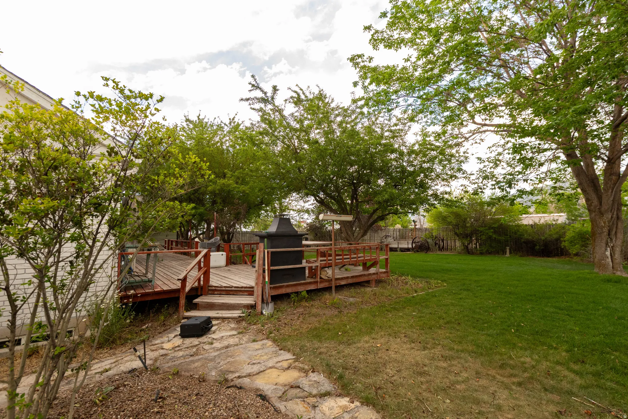 Expansive backyard featuring a large wooden deck with a wooden railing, a sprawling lawn, mature trees, and a stone pathway