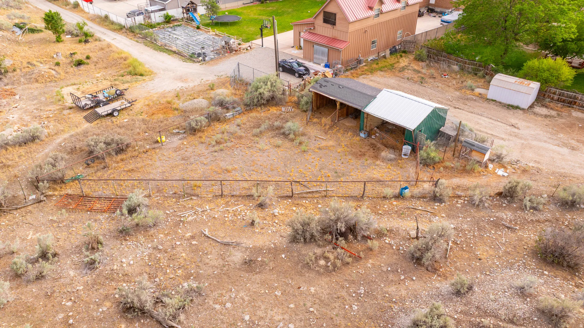Expansive open lot featuring a fenced perimeter, a two-stall covered structure, and additional storage shed