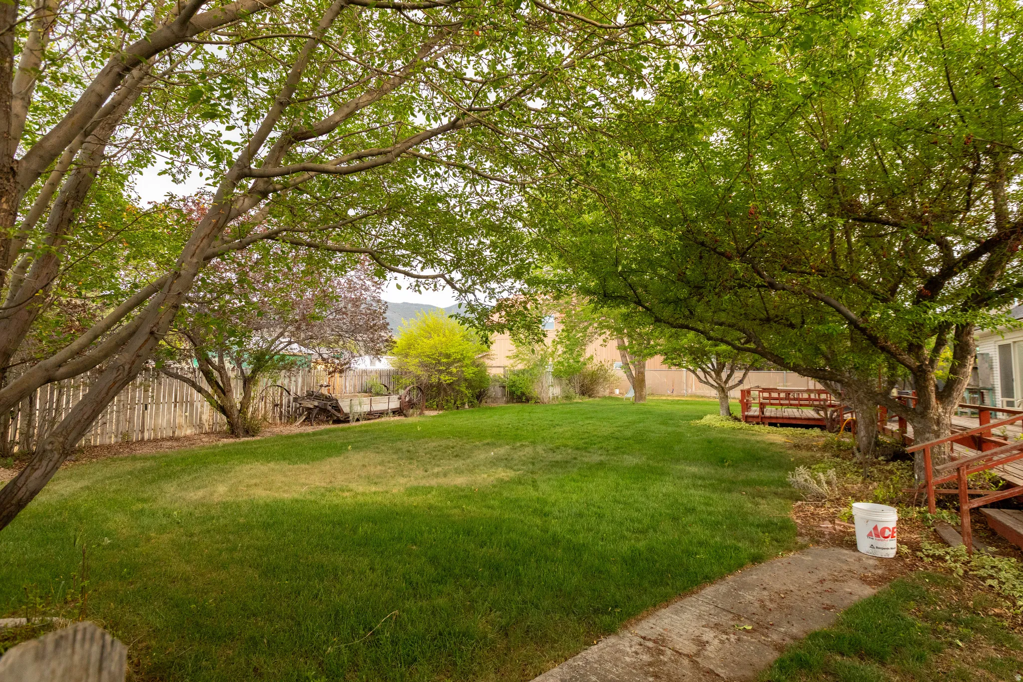 Spacious backyard with mature shade trees, a manicured lawn, wood fencing, and a multi-level wood deck
