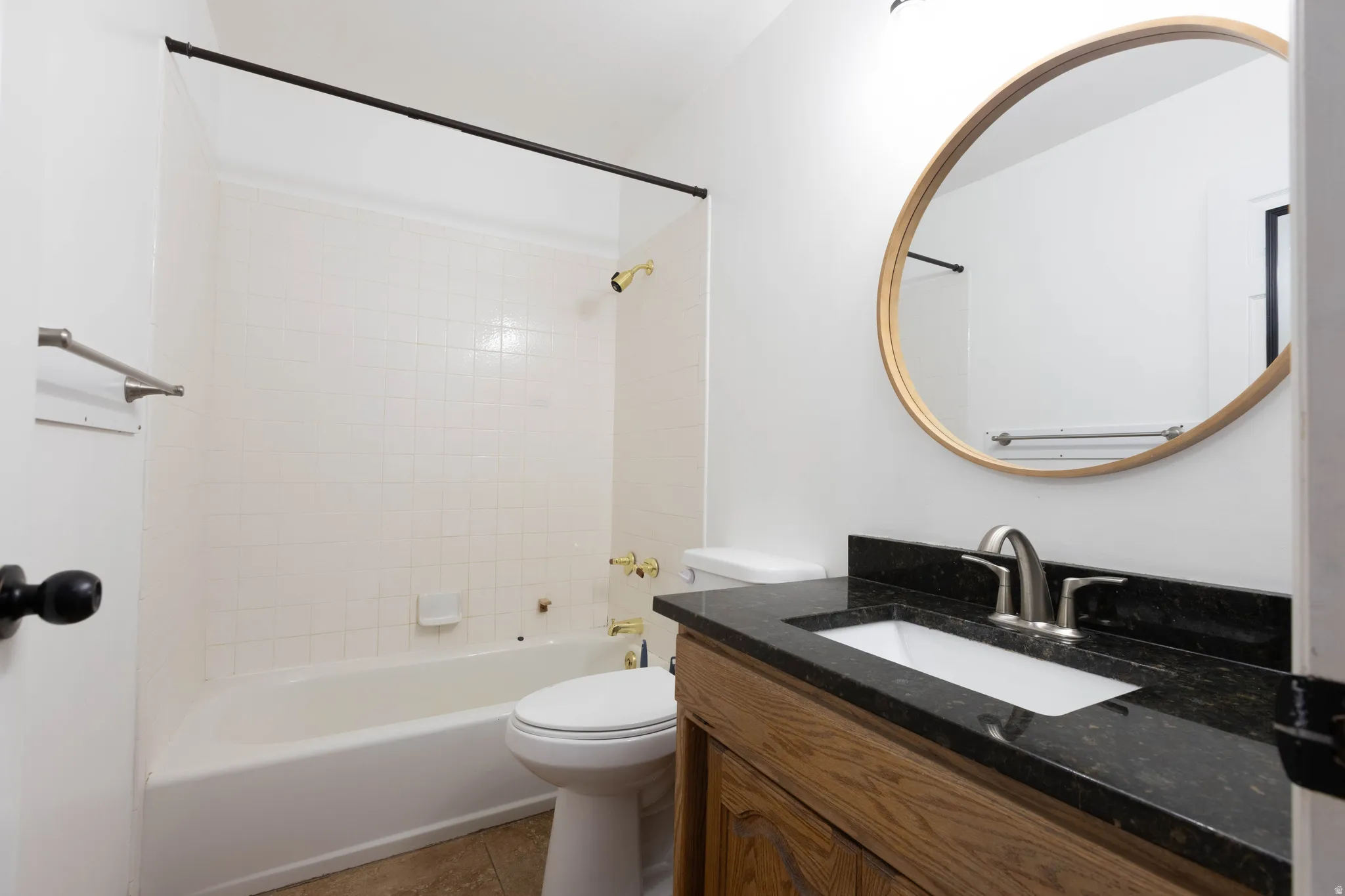 Bathroom featuring a white bathtub, tiled shower surround, wood-finish vanity with a dark countertop, and a circular mirror