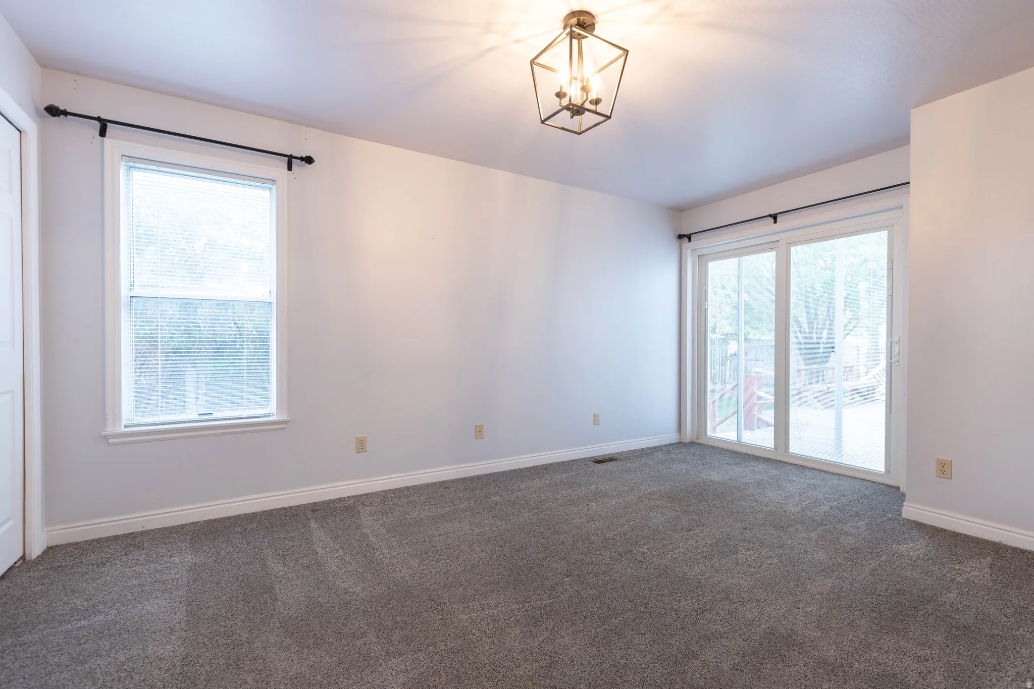Room featuring soft gray carpeting, a window with blinds, and white baseboards