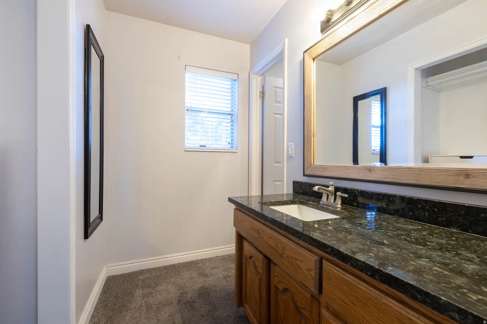 Vanity area featuring a granite-look countertop with an undermount sink, wood-finish cabinetry, and a large framed mirror with overhead lighting