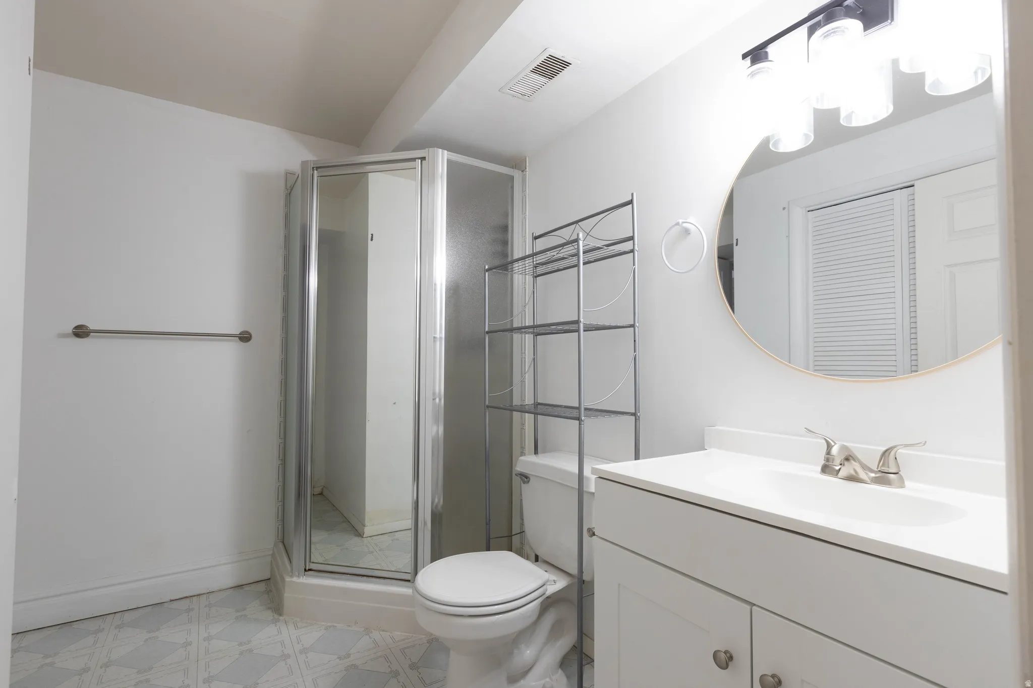Bathroom featuring a corner shower enclosure, white vanity with integrated sink, circular mirror, and overhead vanity lighting