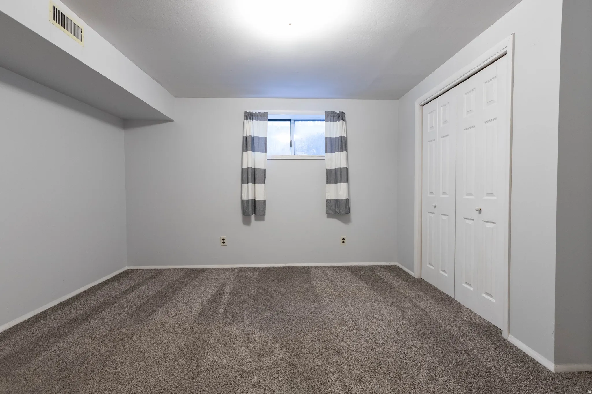Carpeted room featuring a window with white trim, a double bi-fold closet, light gray painted walls, and white baseboards
