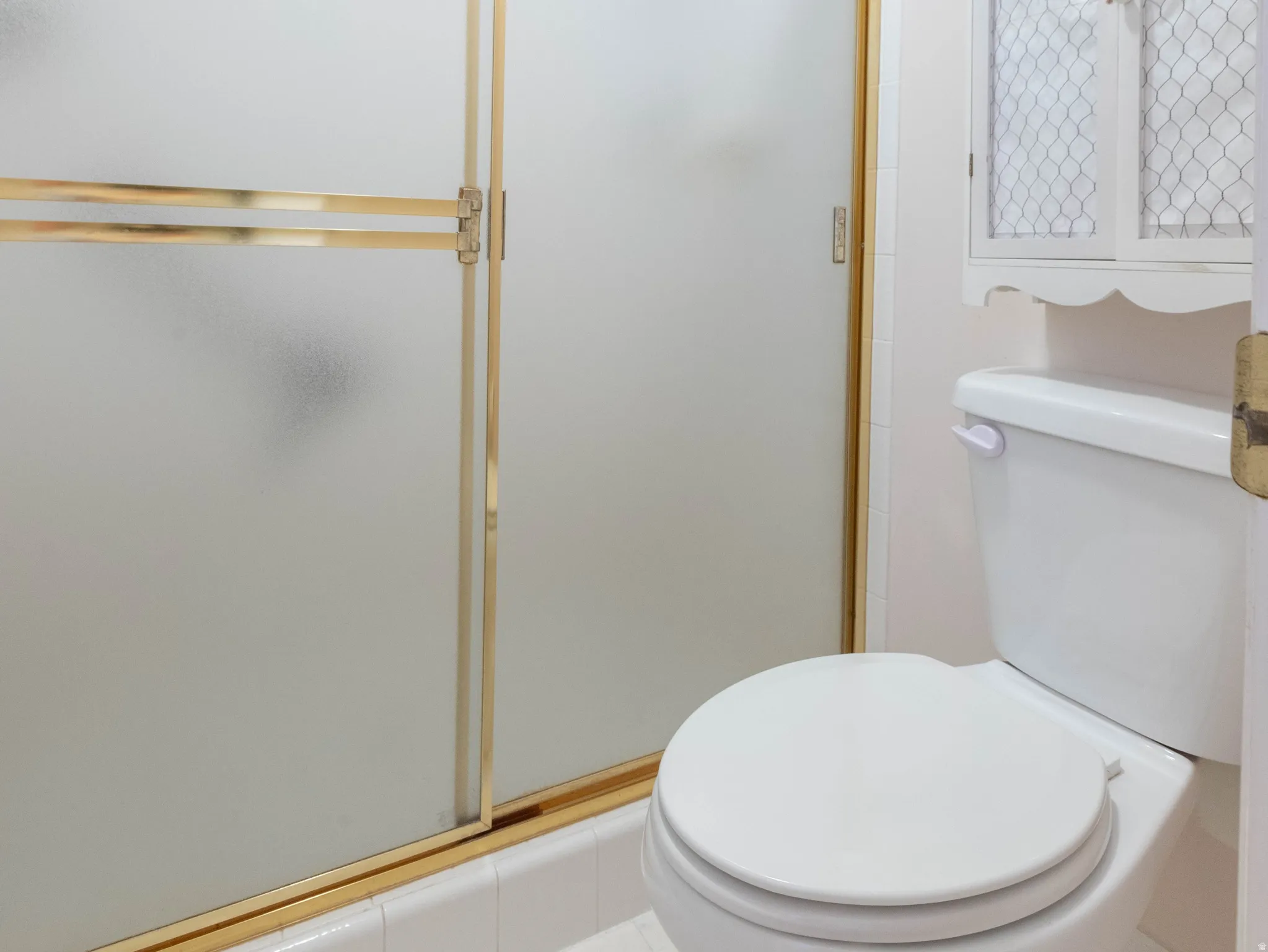 Bathroom featuring a white toilet, white tile flooring, and a shower with frosted glass and a gold-finish frame