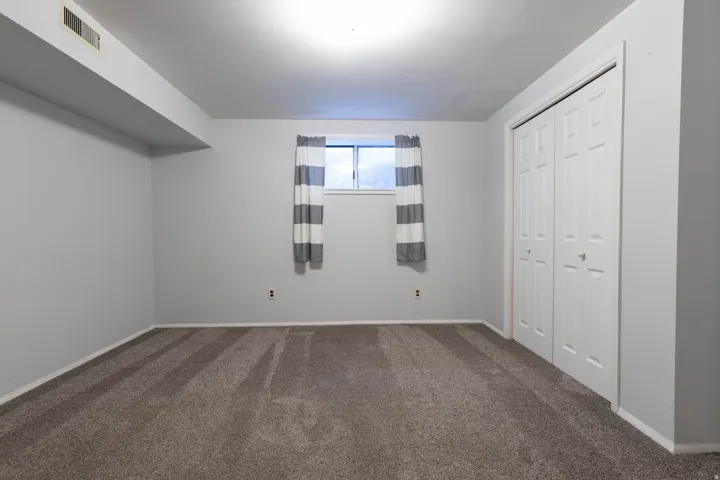 Carpeted room featuring a window with white trim, a double bi-fold closet, light gray painted walls, and white baseboards