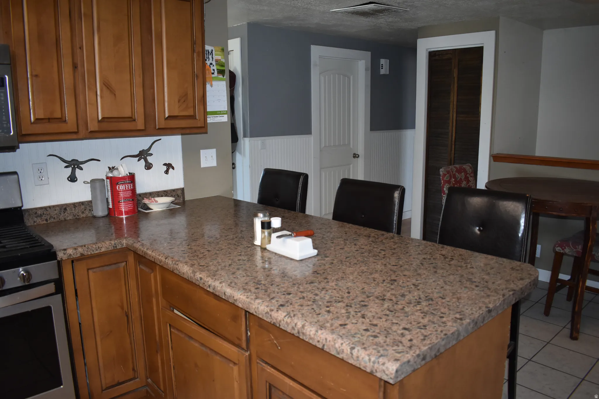 Kitchen featuring a speckled countertop island, wood cabinetry, built-in gas range, and tile flooring