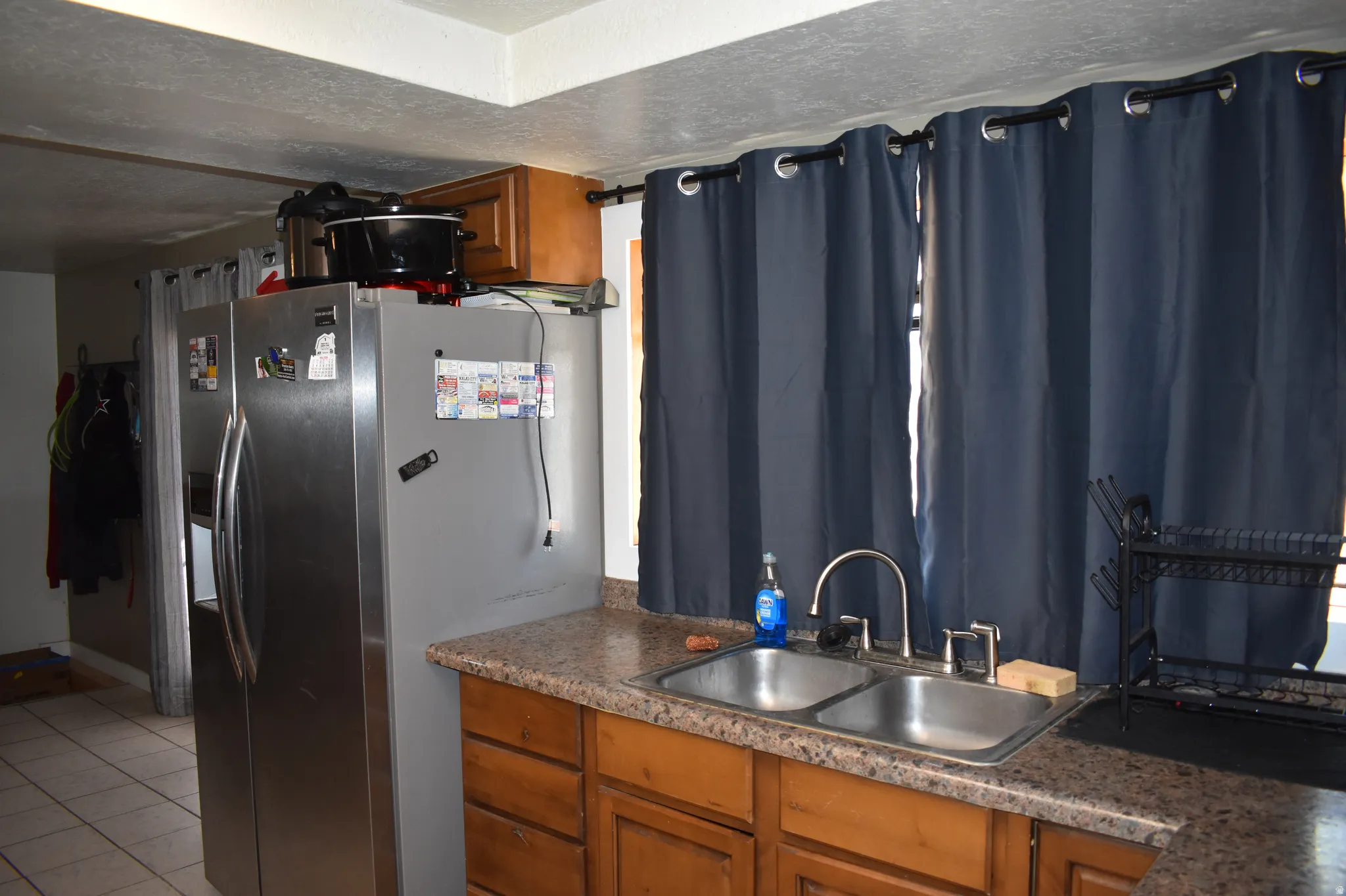 Kitchen area with a double basin stainless steel sink, a stainless steel refrigerator, and wood-finish cabinetry