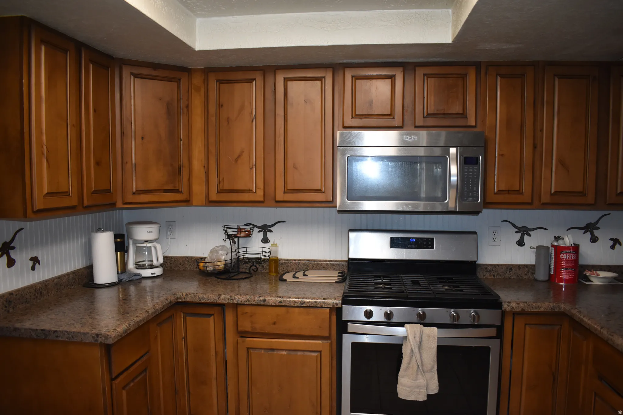 Kitchen featuring extensive wood cabinetry, L-shaped countertops, stainless steel microwave, and a stainless steel range with oven
