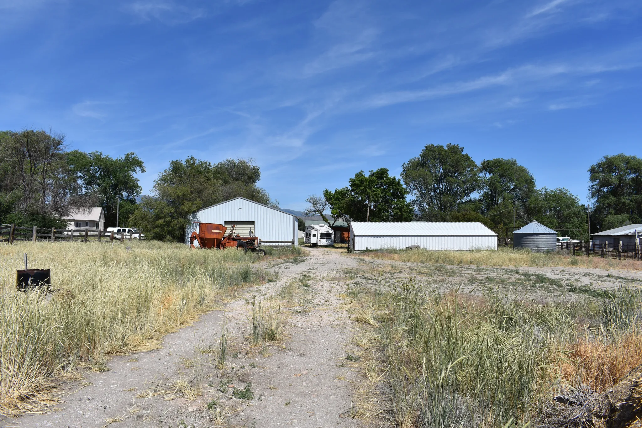 Gravel driveway leading to multiple outbuildings, including a large metal barn and an extended storage structure