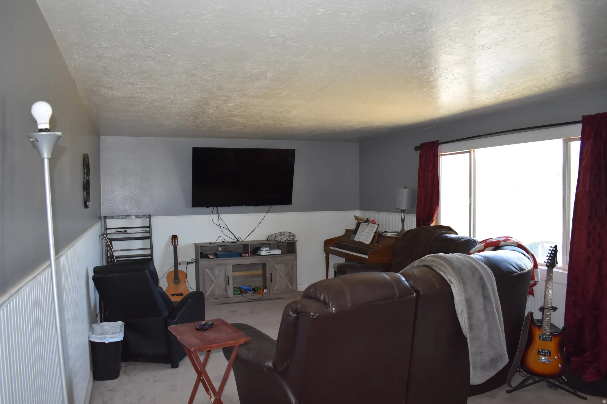 Living area featuring light gray walls with white wainscoting, a large window, and carpeted flooring