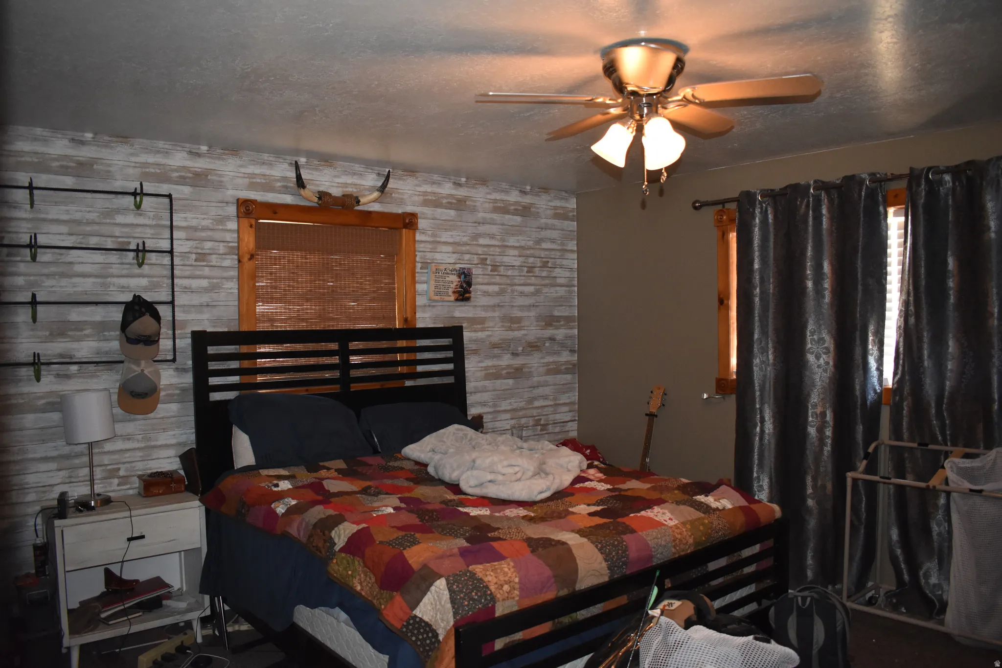 Bedroom featuring a horizontal plank accent wall, wood-trimmed window, and a ceiling fan with integrated lighting