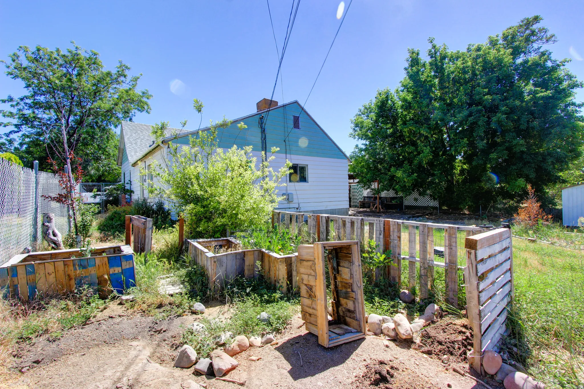 Backyard area featuring wood-constructed garden beds, a privacy fence, and mature trees