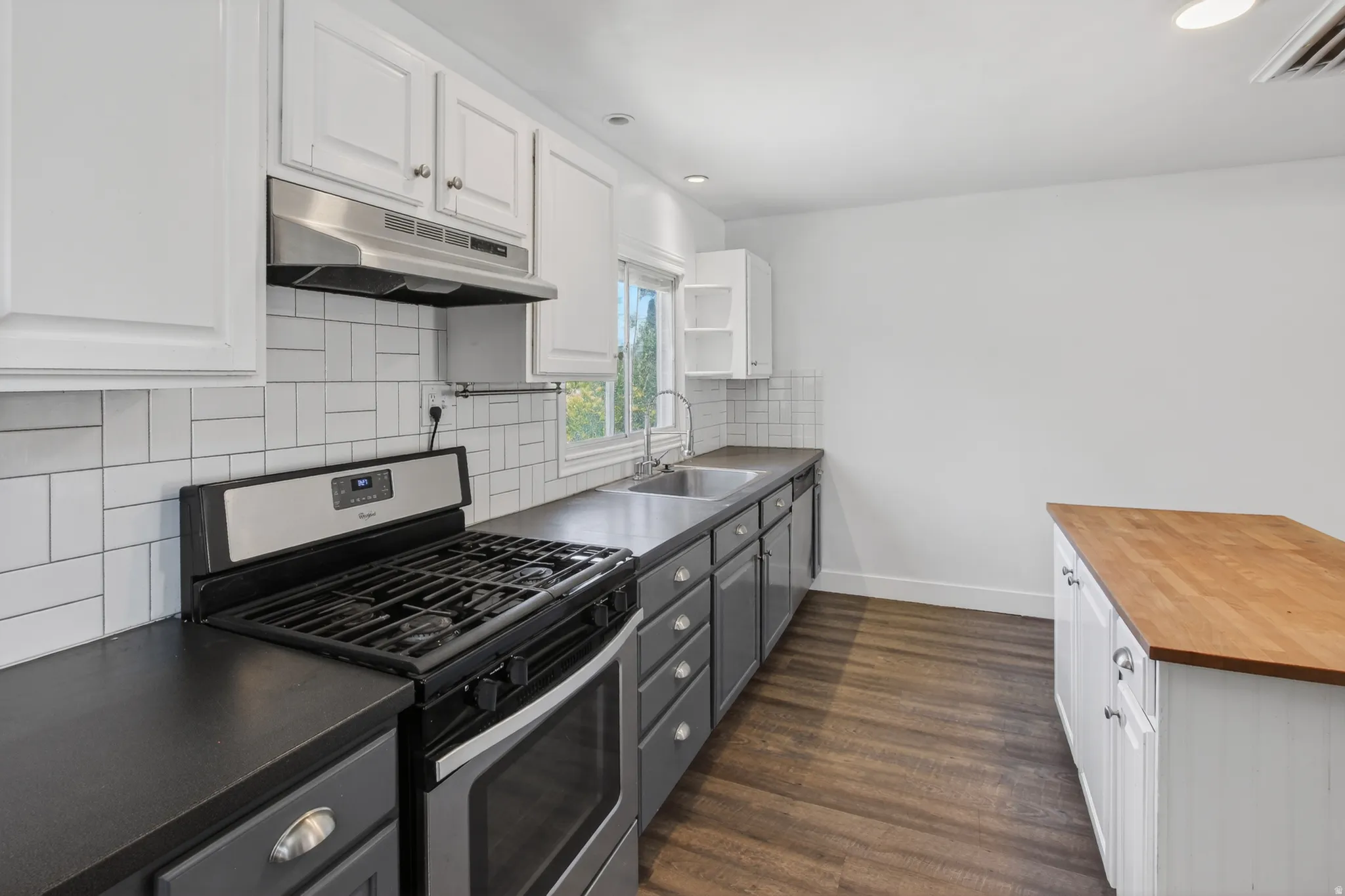 Modern kitchen featuring a stainless steel range, white subway tile backsplash, dark countertops, and wood-finish flooring