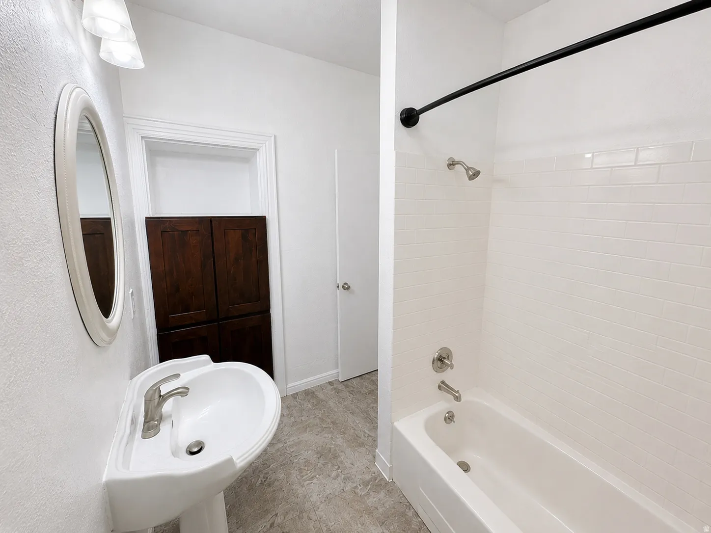 Bathroom with white pedestal sink, brushed nickel faucet, and oval mirror