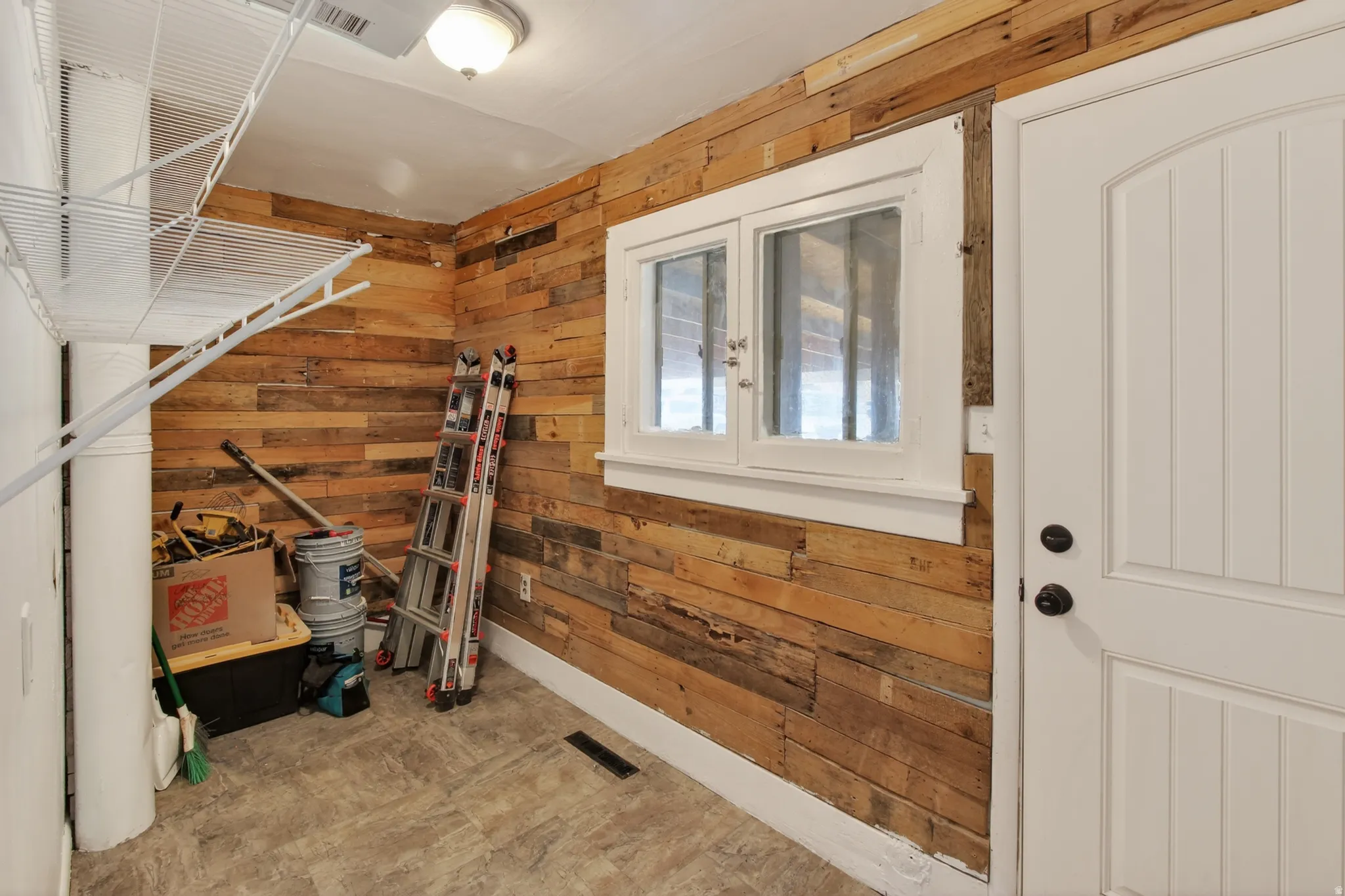 Utility space featuring wood-finish paneling, durable tile flooring, and a white paneled door with black hardware