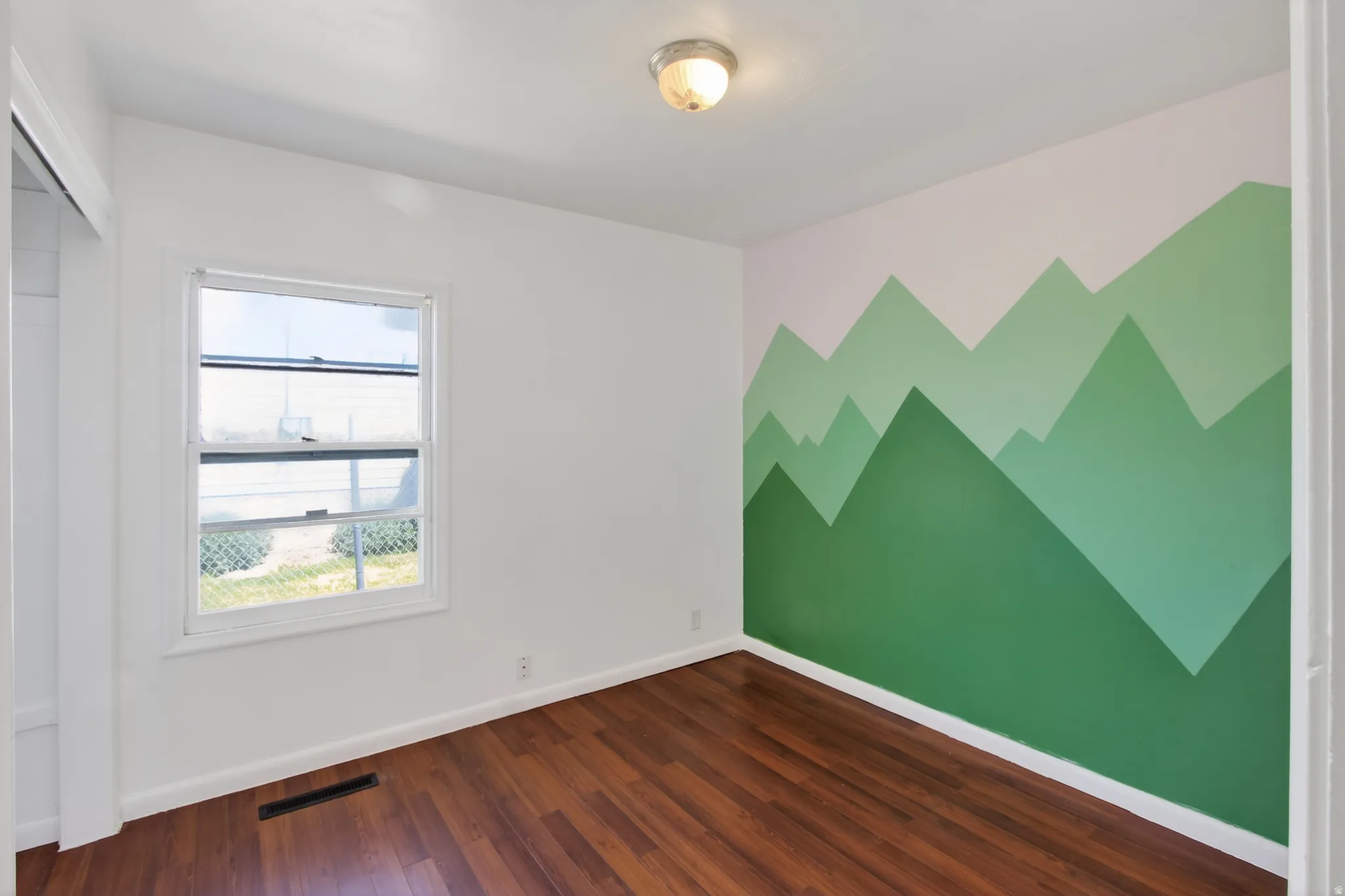 Room featuring a decorative mountain mural accent wall, wood-finish flooring, a double-hung window, white baseboards, and a semi-flush mount ceiling light