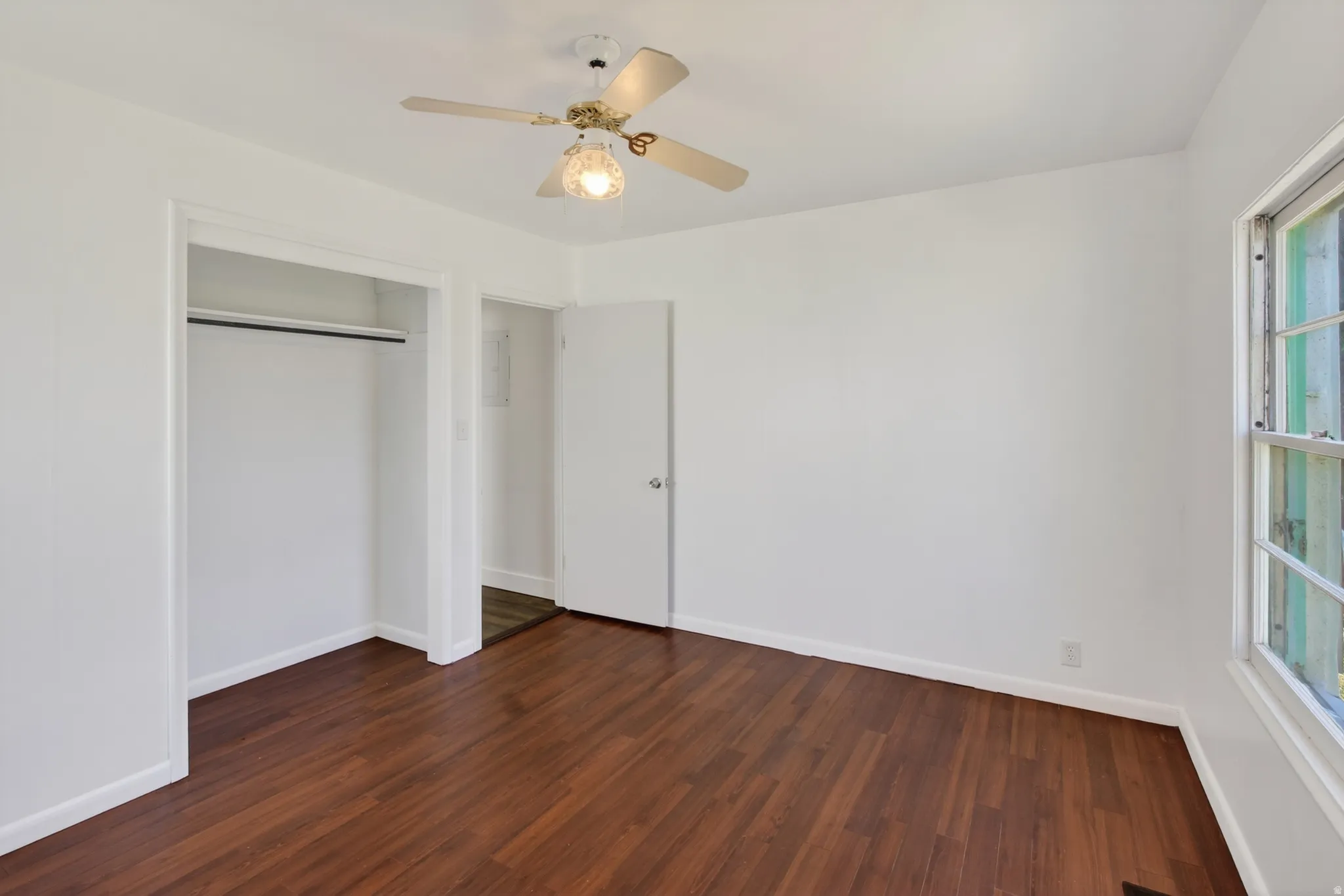 Interior room featuring wood-finish flooring, white walls, and a ceiling fan with light fixture