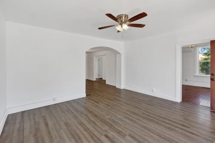 Spacious interior featuring wood-finish flooring, an arched doorway, and a ceiling fan with integrated lighting