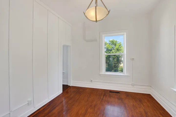 Bright room featuring rich wood-finish flooring, white trim, and a window with natural light