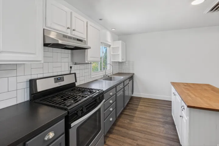 Modern kitchen featuring a stainless steel range, white subway tile backsplash, dark countertops, and wood-finish flooring