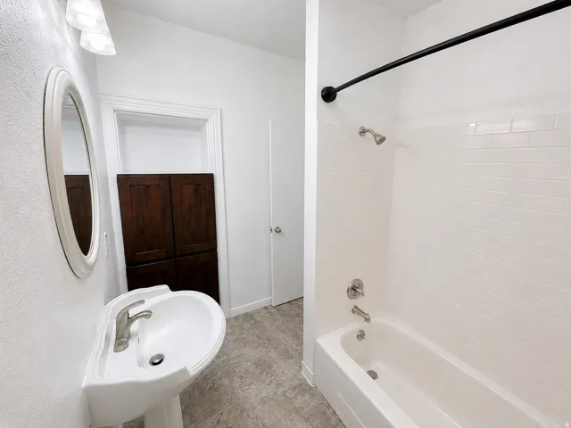 Bathroom with white pedestal sink, brushed nickel faucet, and oval mirror