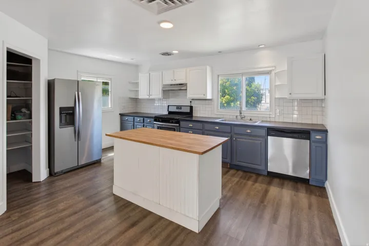 Kitchen featuring wood-finish flooring, a central island with a butcher block countertop, two-tone cabinetry, stainless steel appliances, and a tiled backsplash