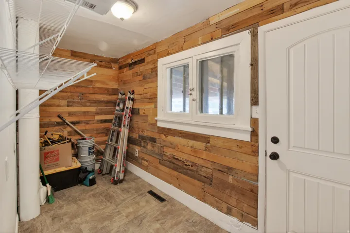 Utility space featuring wood-finish paneling, durable tile flooring, and a white paneled door with black hardware