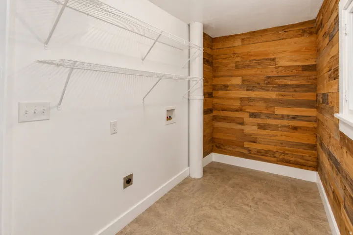 Laundry area featuring a wood-finish accent wall, wire shelving, and an exposed utility pipe