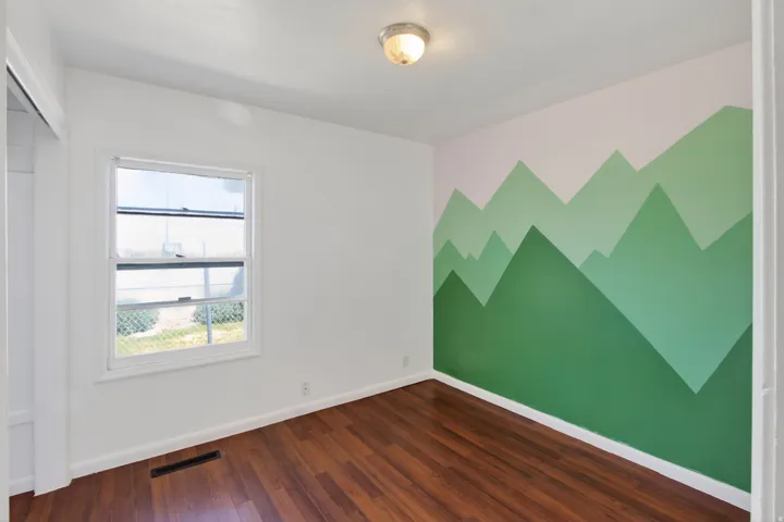 Room featuring a decorative mountain mural accent wall, wood-finish flooring, a double-hung window, white baseboards, and a semi-flush mount ceiling light