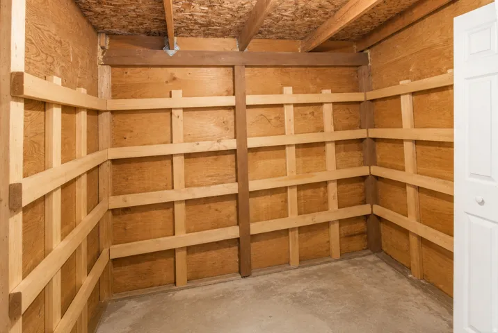 Utility room featuring raw wood paneling, wood slat shelving supports, exposed ceiling joists, particle board ceiling, and a concrete floor