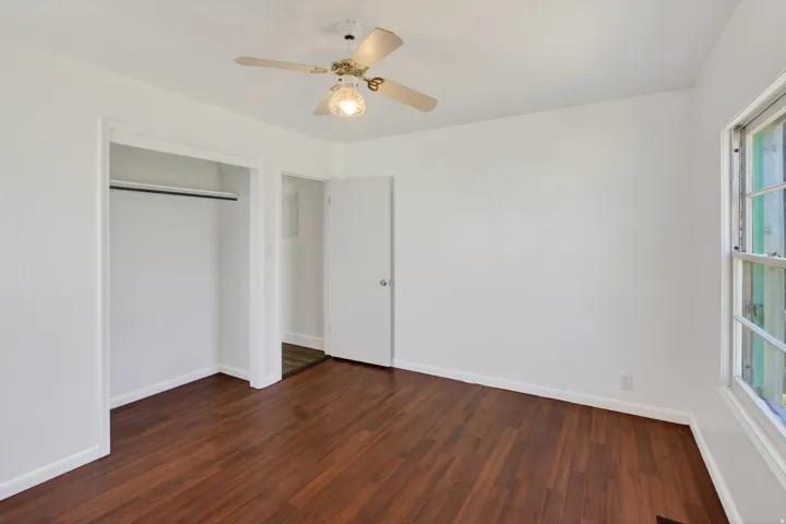 Interior room featuring wood-finish flooring, white walls, and a ceiling fan with light fixture