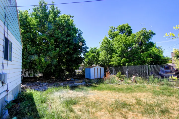 Expansive backyard featuring a metal storage shed, mature trees, chain-link fencing, and white lattice fencing
