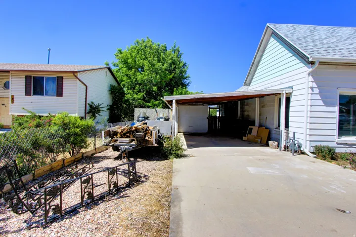 Side of property featuring a covered carport, light blue horizontal siding, and a sloped, graveled yard area with a chain-link fence