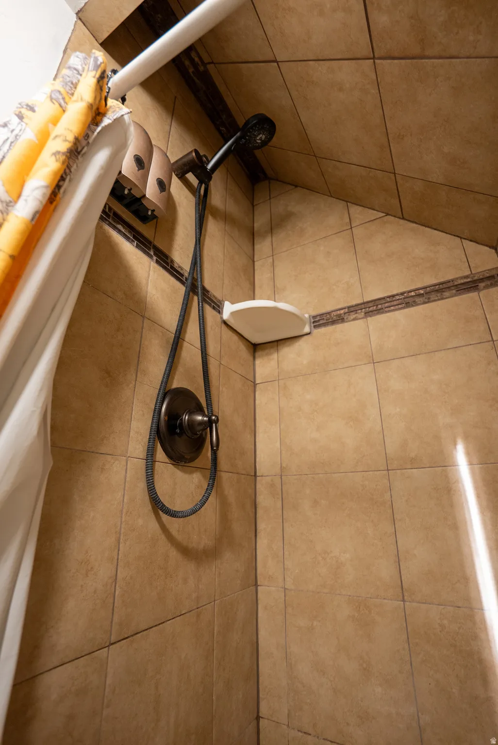 Tiled shower surround featuring a bronze showerhead and control handle, a corner shelf, and a decorative accent tile band