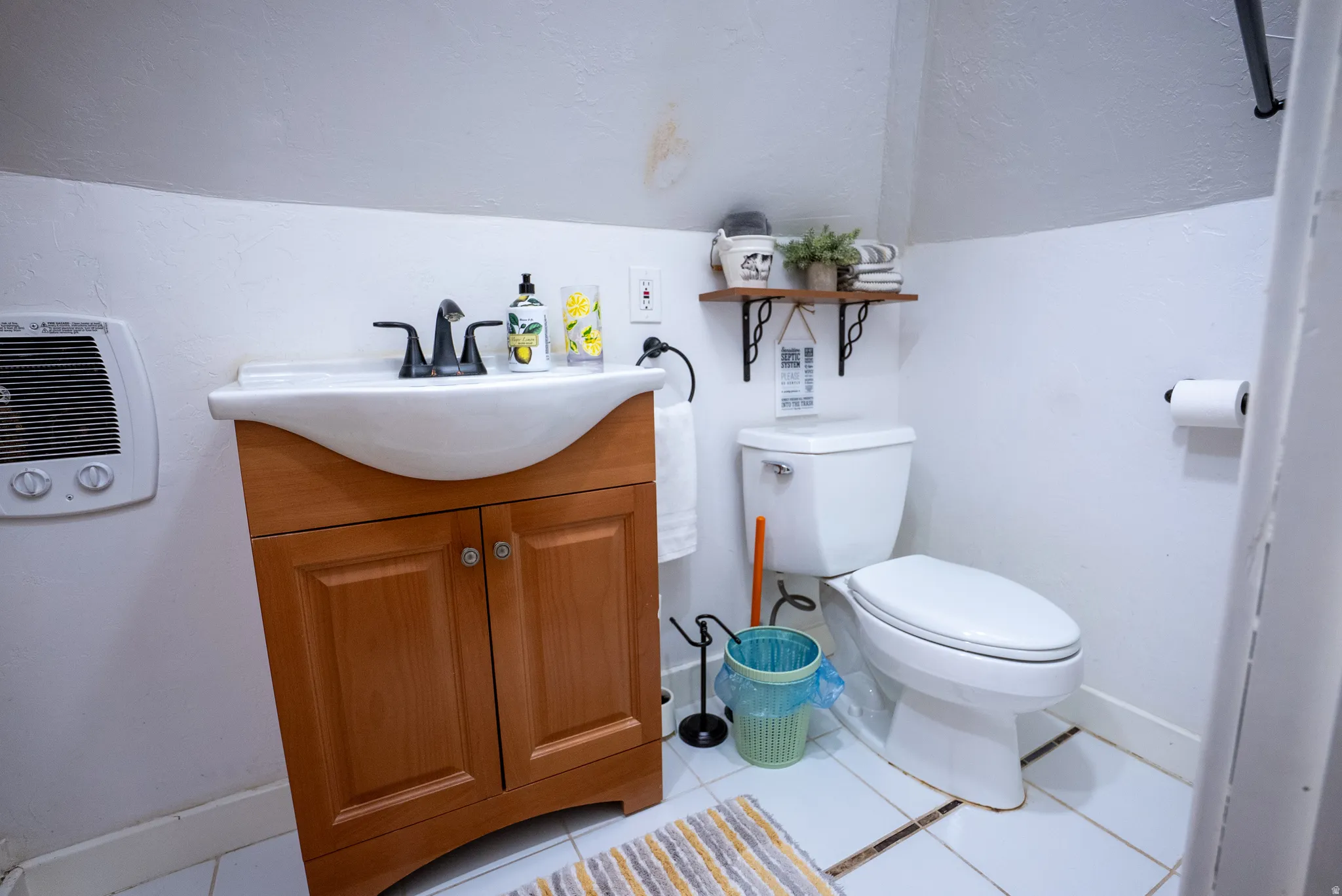 Bathroom featuring a wooden vanity with integrated sink, a white toilet, and white tile flooring