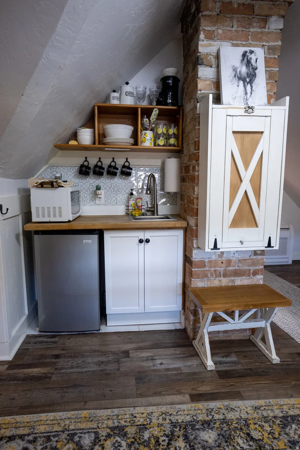 Compact kitchen area featuring wood-finish flooring, white cabinetry, and a stainless steel undercounter refrigerator