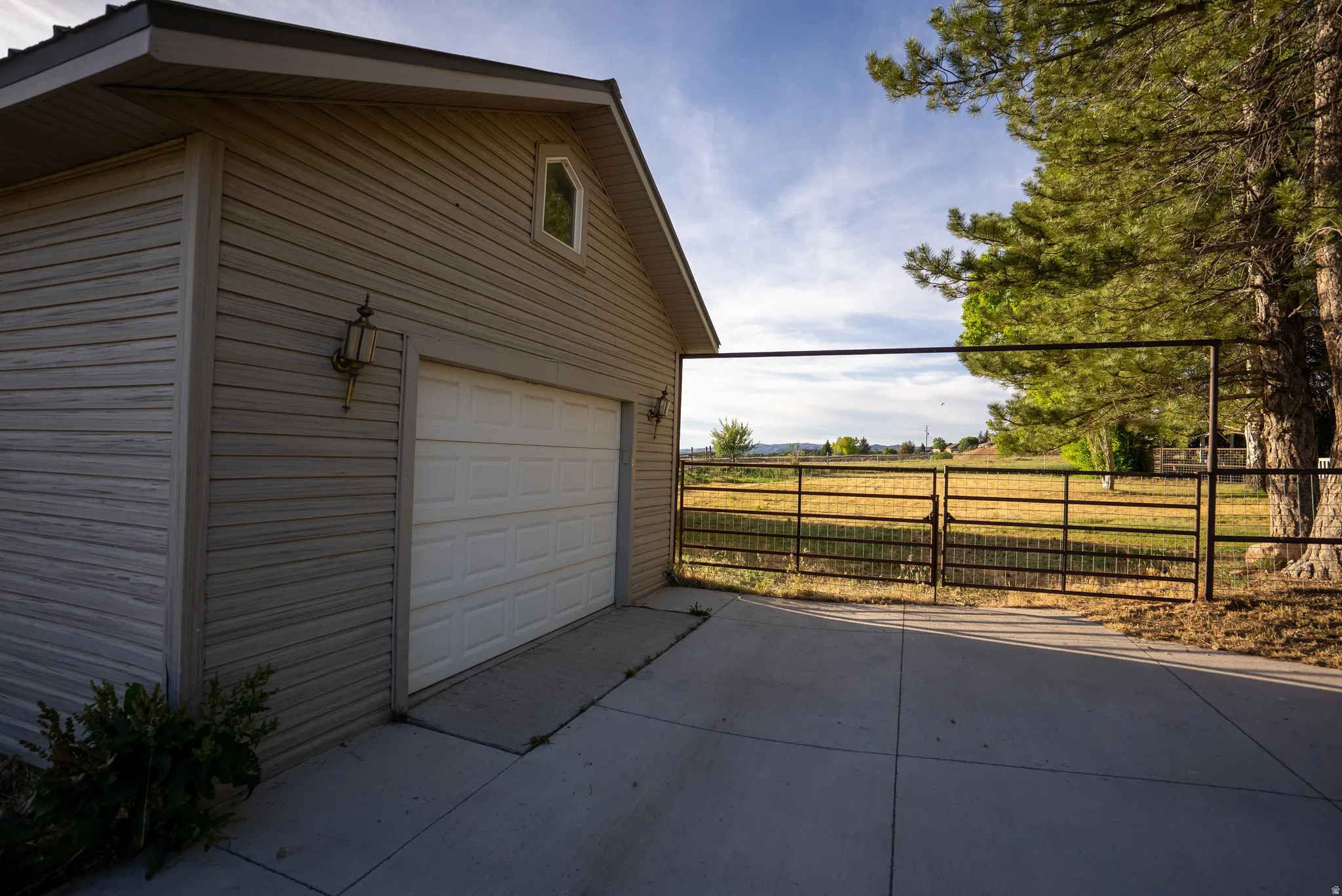 Two-car garage with horizontal siding, featuring an arched window, decorative outdoor lighting, and a concrete driveway