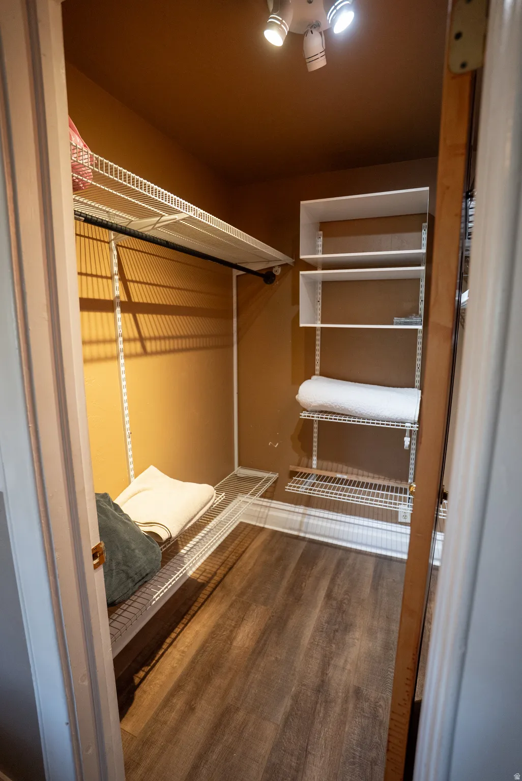 Walk-in closet featuring wood-finish flooring, adjustable wire shelving, built-in rod, and track lighting