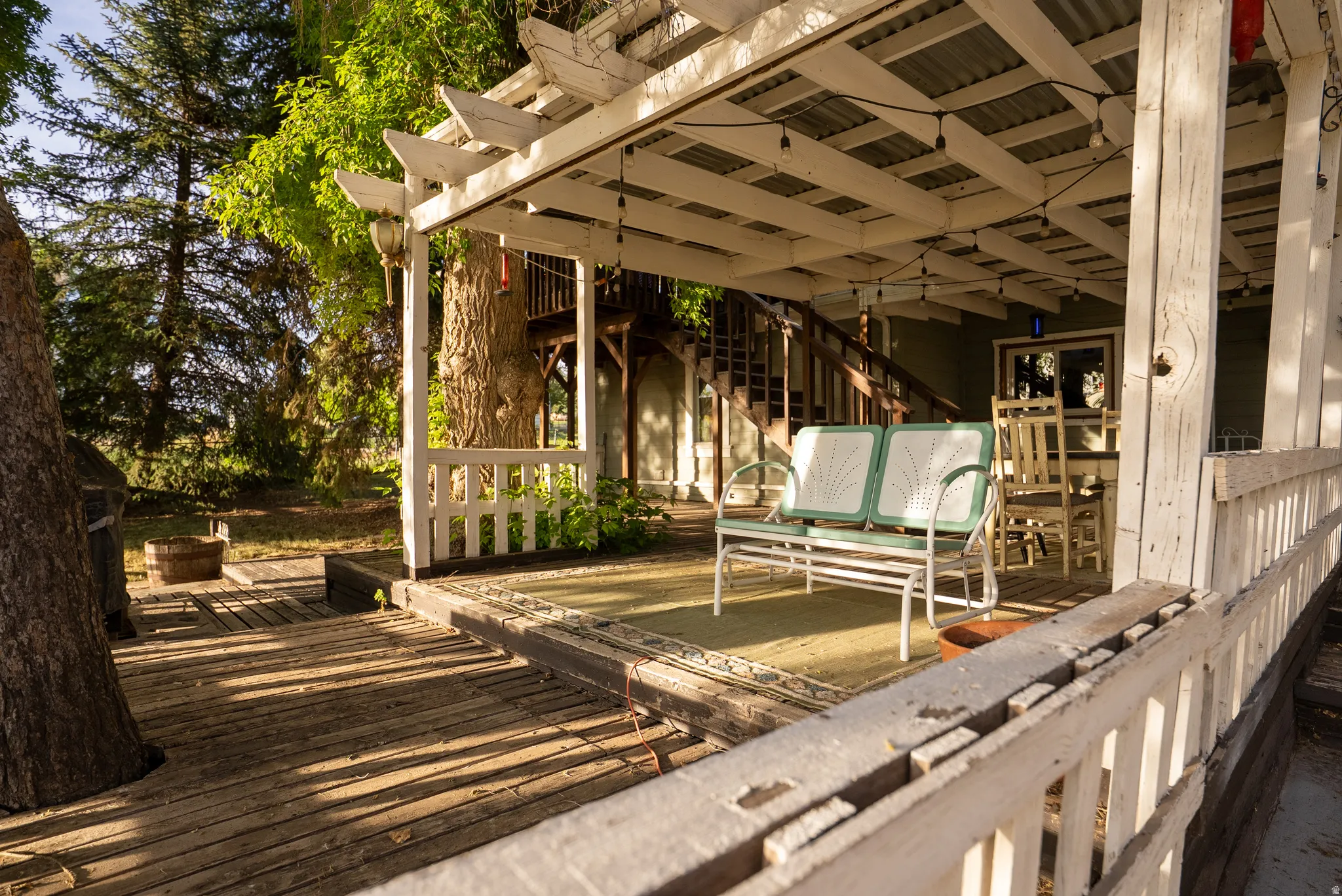 Expansive outdoor decking featuring a covered patio with string lighting, painted wooden railing, and a visible exterior staircase