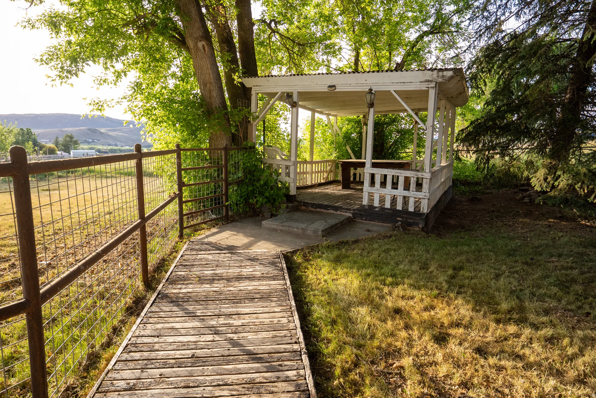 Wood plank pathway leading to a white gazebo with a built-in bench
