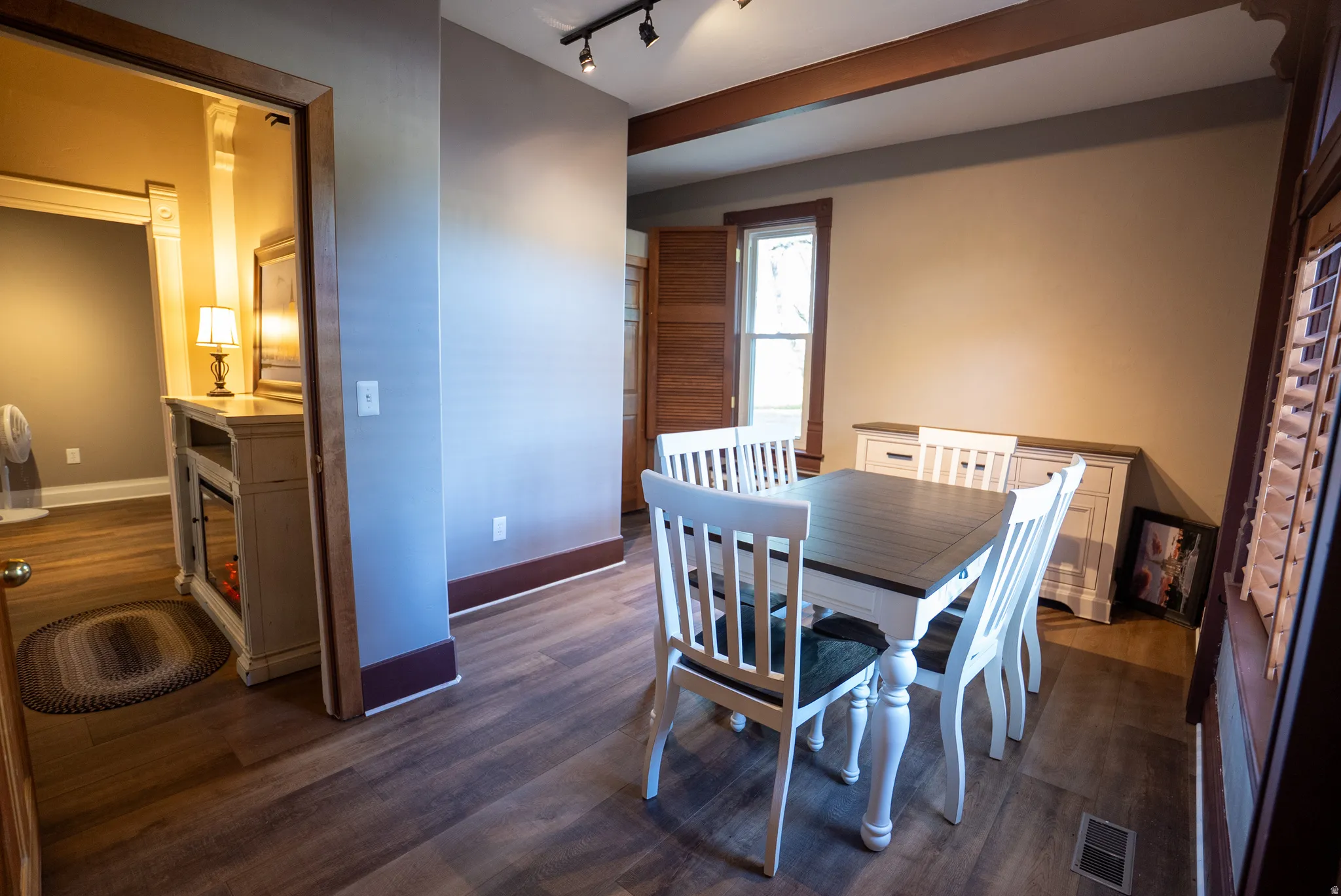 Dining area featuring wood-finish flooring, exposed ceiling beams, and a window with plantation shutters
